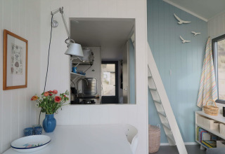 Bright, cozy interior of Beach house 'Dishoek 60' with flowers, blue wall, and kitchen pass-through window.