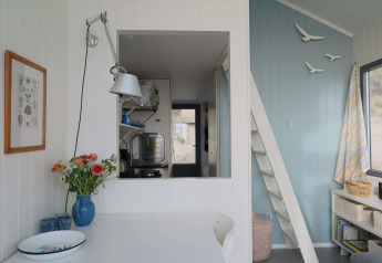 Interior luminoso y acogedor de Beach house 'Dishoek 60' con flores, pared azul y ventana hacia la cocina.