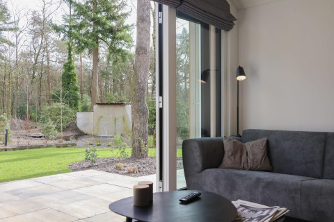 Sala en Forest Lodge, De Hooge Veluwe, Países Bajos, con vista a la terraza y el bosque desde la puerta abierta.