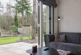 Sala en Forest Lodge, De Hooge Veluwe, Países Bajos, con vista a la terraza y el bosque desde la puerta abierta.