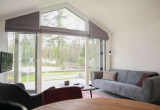 Wohnbereich der Forest Lodge im De Hooge Veluwe, Niederlande, mit großen Fenstern und Waldblick