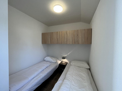 Zwei Einzelbetten in einem schlichten Zimmer mit weißer Bettwäsche, Nachttisch und Schrank im Forest Lodge bei De Hooge Veluwe.