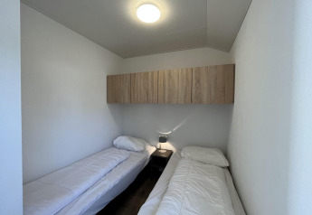 Zwei Einzelbetten in einem schlichten Zimmer mit weißer Bettwäsche, Nachttisch und Schrank im Forest Lodge bei De Hooge Veluwe.
