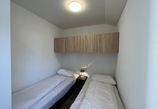 Habitación pequeña con dos camas individuales, ropa de cama blanca y armario en Forest Lodge en De Hooge Veluwe.