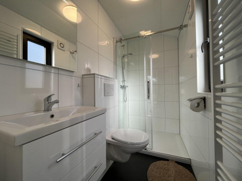 Baño moderno con ducha acristalada, inodoro suspendido y lavabo en Forest Lodge, De Hooge Veluwe, Países Bajos.