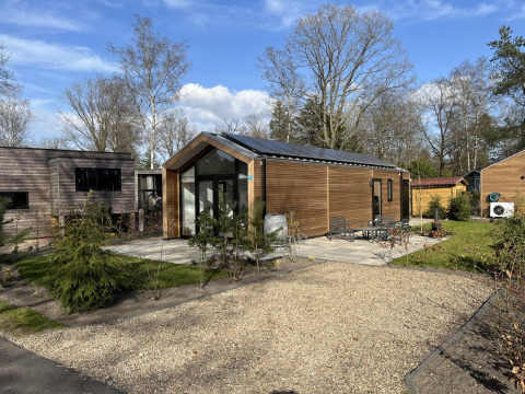 Moderna cabaña Forest Lodge en De Hooge Veluwe, Países Bajos, rodeada de árboles y patio con muebles exteriores.