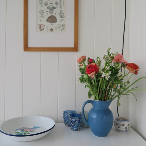 Indretning i strandhus med blomster i en blå kande, skåle og billedramme på væg i Zeeland, Dishoek.