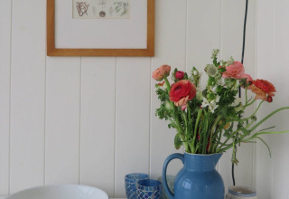 Strandhuisdecoratie met een blauwe kan bloemen, kommen en een kader aan de muur in Dishoek, Zeeland.
