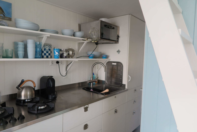 Moderne Küche im Beach house 'Dishoek 60' mit weißen Regalen und Edelstahlplatte in Zeeland.