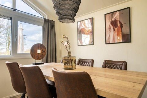 Coin repas d’un lodge avec chaises brunes modernes, table en bois, grandes fenêtres et œuvres murales.