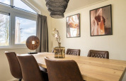 Eethoek in een lodge met moderne bruine stoelen, houten tafel, grote ramen en kunst aan de muur.