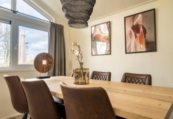 Sala da pranzo in un lodge con sedie moderne marroni, tavolo in legno, ampie finestre e arte sulla parete.