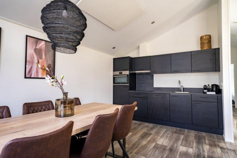 Moderne lodgekeuken en eetruimte met donkere kasten, houten tafel, leren stoelen en decoraties.