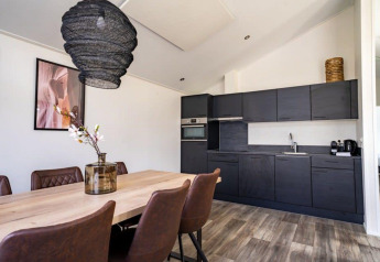 Moderne lodgekeuken en eetruimte met zwarte kasten, houten tafel, lederen stoelen en decoratie.