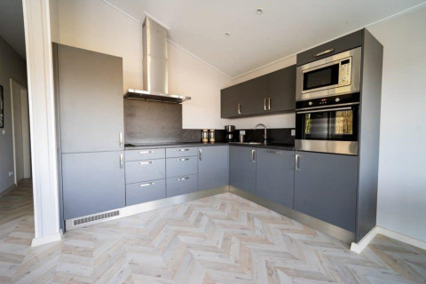 Cocina de cabaña moderna con gabinetes grises, electrodomésticos integrados y suelo en espiga clara.