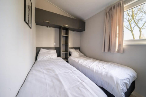 Dormitorio de lodge con dos camas individuales, ropa de cama blanca, ventana con cortinas y armarios arriba.
