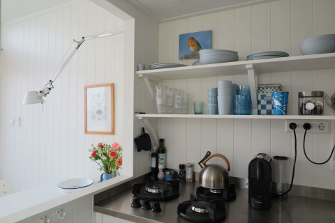 Moderne strandhus-køkken i Dishoek 60 med åbne hylder, gasblus, elkedel og blå service.