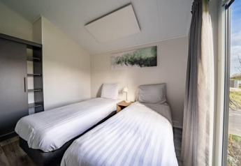 Et moderne lodge-værelse med to enkeltsenge, et natbord, garderobe og stort vindue med udsigt udenfor.
