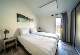 Dormitorio moderno de lodge con dos camas individuales, mesita, lámparas, arte en la pared y ventana con cortinas.