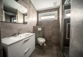 Baño moderno en una posada con azulejos grises, inodoro suspendido, espejo grande y ducha independiente.