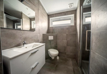 Moderne badkamer in een lodge met grijze tegels, hangtoilet, grote spiegel en aparte doucheruimte.