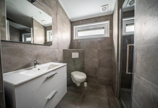 Moderne badkamer in een lodge met grijze tegels, hangtoilet, grote spiegel en aparte doucheruimte.