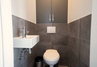 Baño moderno y compacto en un lodge con inodoro suspendido, pequeño lavabo y paredes de azulejos grises.