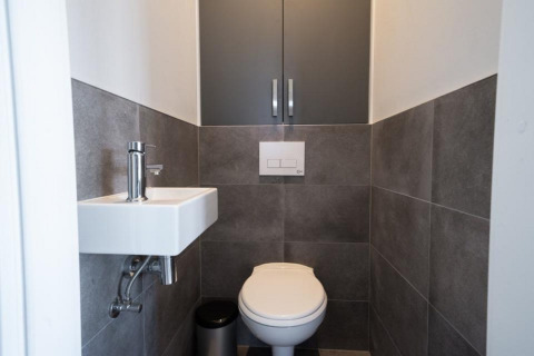 Petite salle de bain moderne de lodge avec WC mural, petit lavabo, et murs carrelés gris.