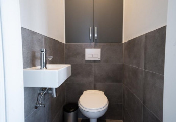 Baño moderno y compacto en un lodge con inodoro suspendido, pequeño lavabo y paredes de azulejos grises.