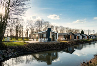 Lodge moderno junto a un canal, con cabañas similares y árboles sin hojas en un día soleado.