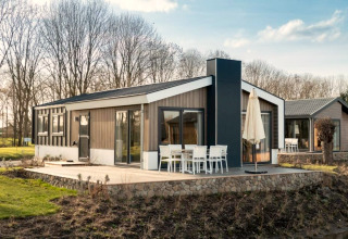 Lodge moderno con grandes ventanales y terraza al aire libre, con zona de comedor, rodeado de árboles y naturaleza.