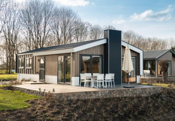 Lodge moderne avec grandes fenêtres et terrasse extérieure avec coin repas, entouré d'arbres et de verdure.