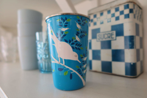 Vaso azul con dibujo de pájaros frente a una lata de 'Sucre' en Beach house Dishoek 60, Zeeland, Países Bajos.