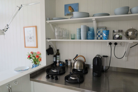 Lyst køkken i strandhuset Dishoek 60 med åbne hylder, gaskomfur, elkedel og kaffemaskine.