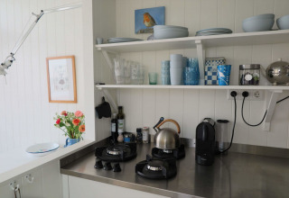 Cucina luminosa della Beach house Dishoek 60, con mensole aperte, fornello a gas, bollitore e macchina da caffè.