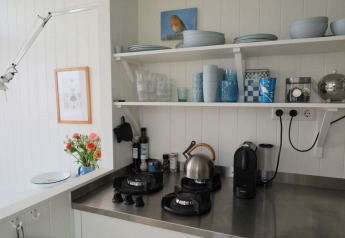 Cuisine lumineuse de la maison de plage Dishoek 60 avec étagères ouvertes, gazinière, bouilloire et cafetière.