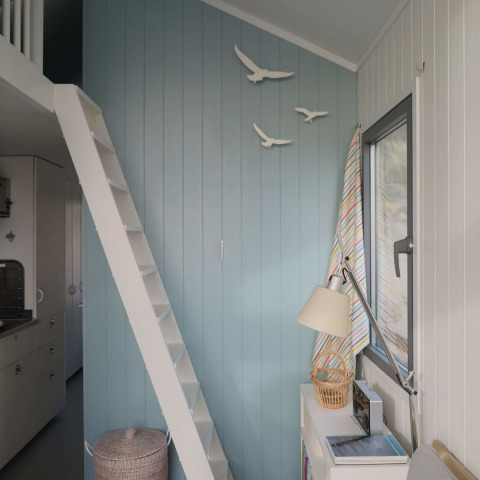 Lyst interiør af strandhus med blå væg, hvid trappe til hems og dekoration af fugle i Zeeland, Nederlandene.