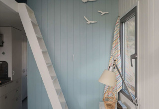 Lyst interiør af strandhus med blå væg, hvid trappe til hems og dekoration af fugle i Zeeland, Nederlandene.