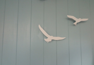Deux décorations blanches d'oiseaux sur un mur bleu clair dans la maison de plage 'Dishoek 60' à Zeeland, Pays-Bas.