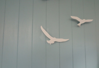 Deux décorations blanches d'oiseaux sur un mur bleu clair dans la maison de plage 'Dishoek 60' à Zeeland, Pays-Bas.