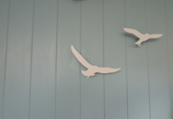 Deux décorations blanches d'oiseaux sur un mur bleu clair dans la maison de plage 'Dishoek 60' à Zeeland, Pays-Bas.