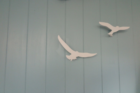 Twee witte vogeldecoraties tegen een lichtblauwe muur in strandhuis ‘Dishoek 60’ in Zeeland, Nederland.