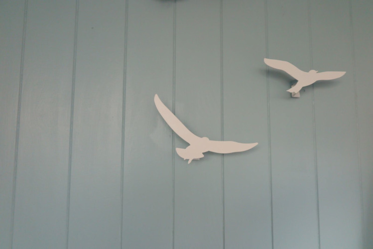 Dos decoraciones blancas de aves en una pared azul claro en la casa de playa 'Dishoek 60' en Zeeland, Países Bajos.