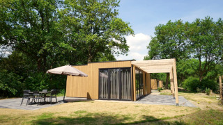 Modern lodge named Cube with wooden exterior, large patio, and outdoor seating surrounded by green trees.