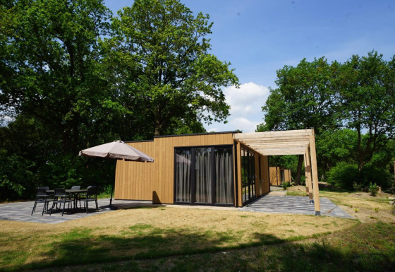 Moderno lodge chiamato Cube con esterno in legno, ampio patio e posti a sedere all’aperto tra gli alberi.