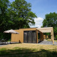 Moderne Lodge namens Cube mit Holzfassade, Terrasse und Sitzbereich im Grünen, umgeben von Bäumen.