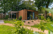 Moderna cabaña Cube en EuroParcs Ruinen, Países Bajos, rodeada de vegetación y árboles al aire libre.
