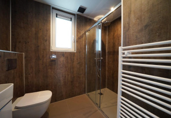 Modern bathroom with wood-style walls, glass shower and window at the Cube in EuroParcs Ruinen, Netherlands.