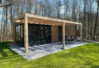 Modern Cube lodge at EuroParcs Ruinen, Netherlands, with glass walls, wood pergola, and forest view.