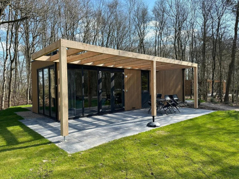Moderne Cube-Lodge im EuroParcs Ruinen, Niederlande, mit Glasfront, Holzpergola und Waldblick.